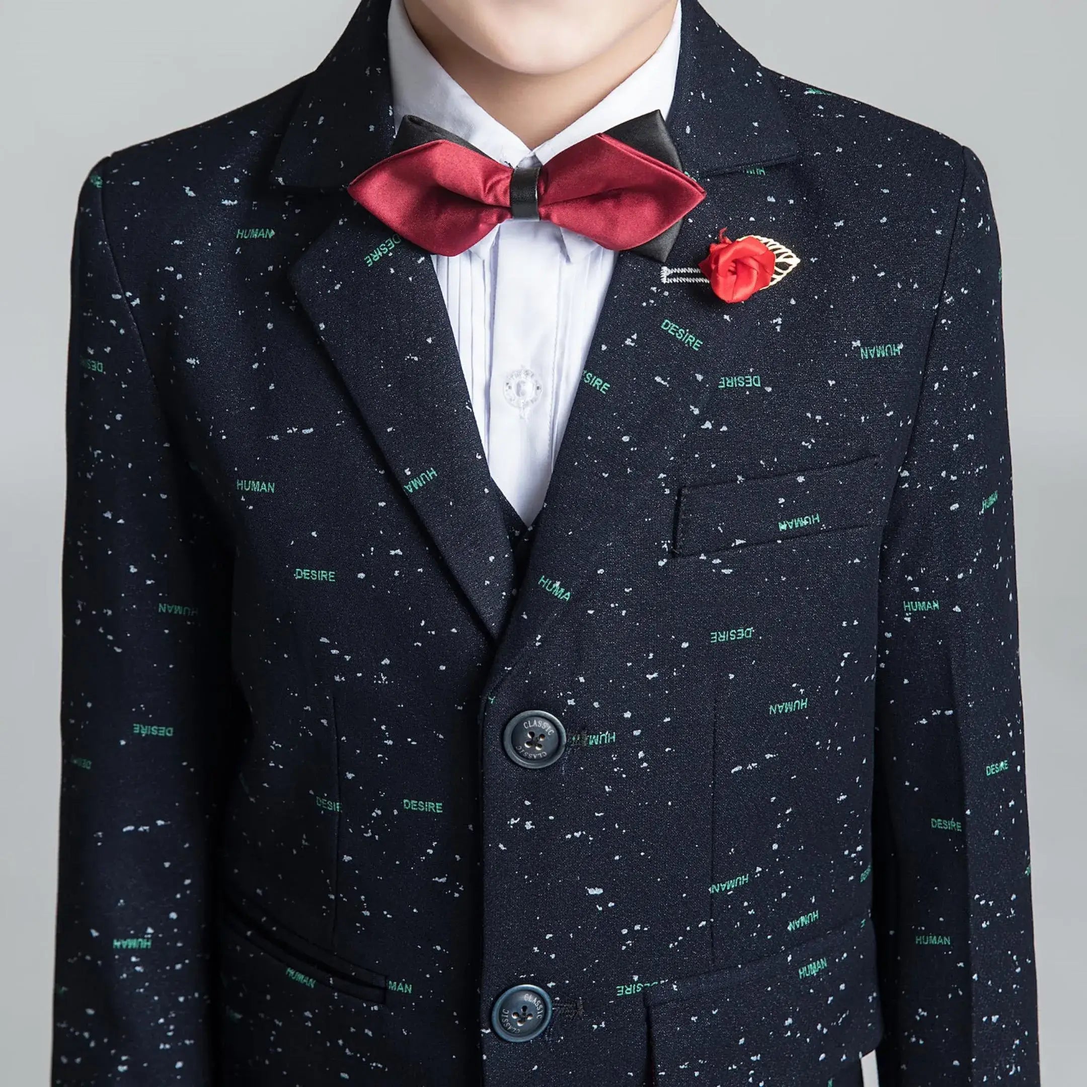 Close-up of boys' printed suit jacket with red bow tie and lapel pin, tailored for formal parties and festive events