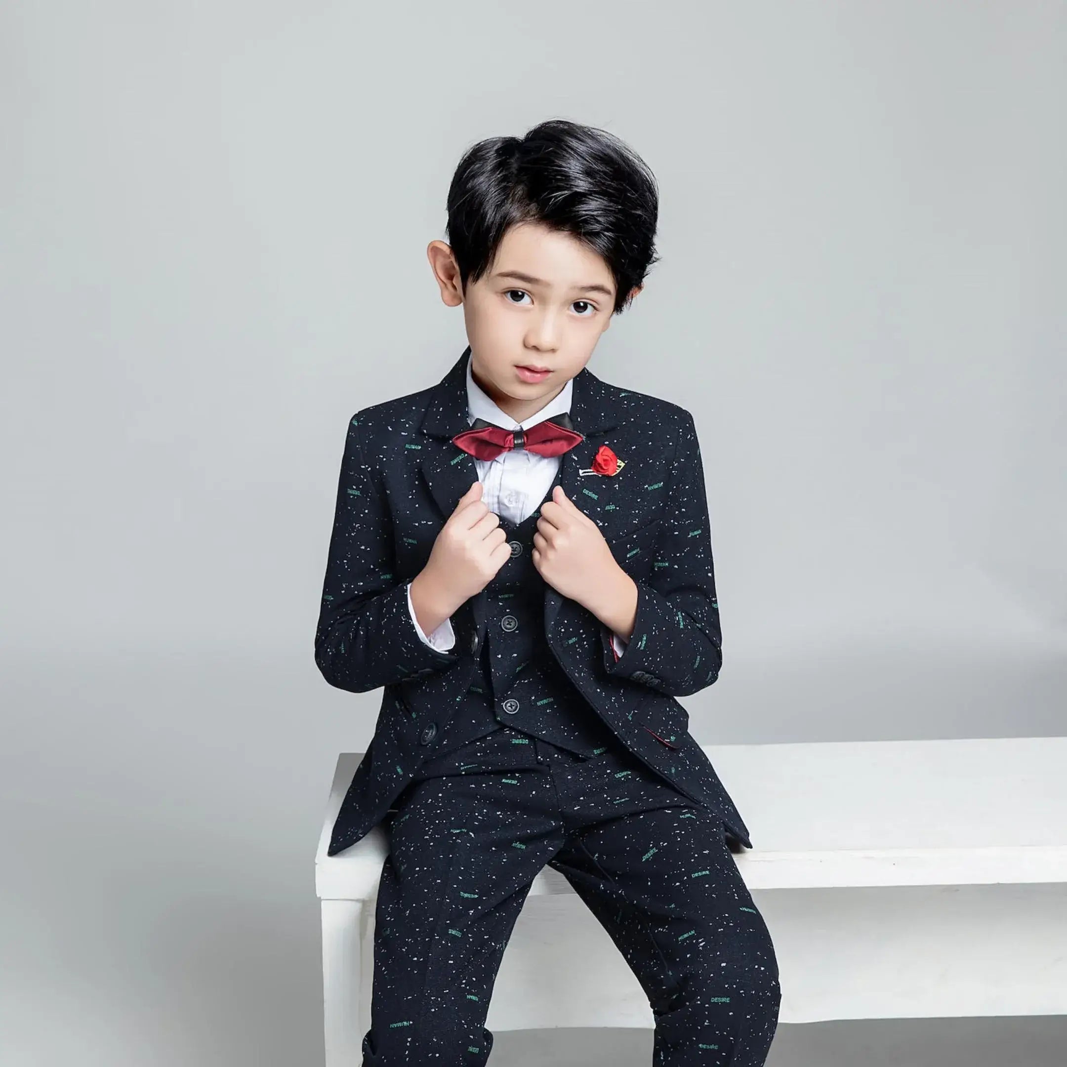 Printed boys' formal suit with red bow tie and rose pin, three-piece outfit styled for weddings or special events