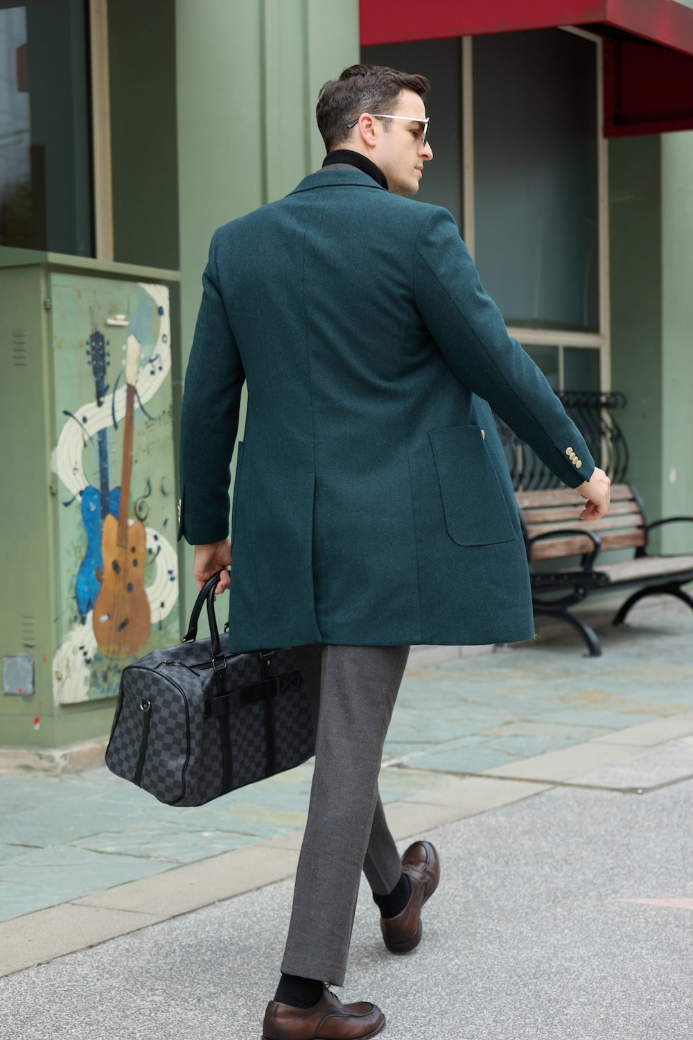 Men's green wool overcoat - back view of double breasted long winter coat with welt pockets, walking in urban street with checked duffle bag