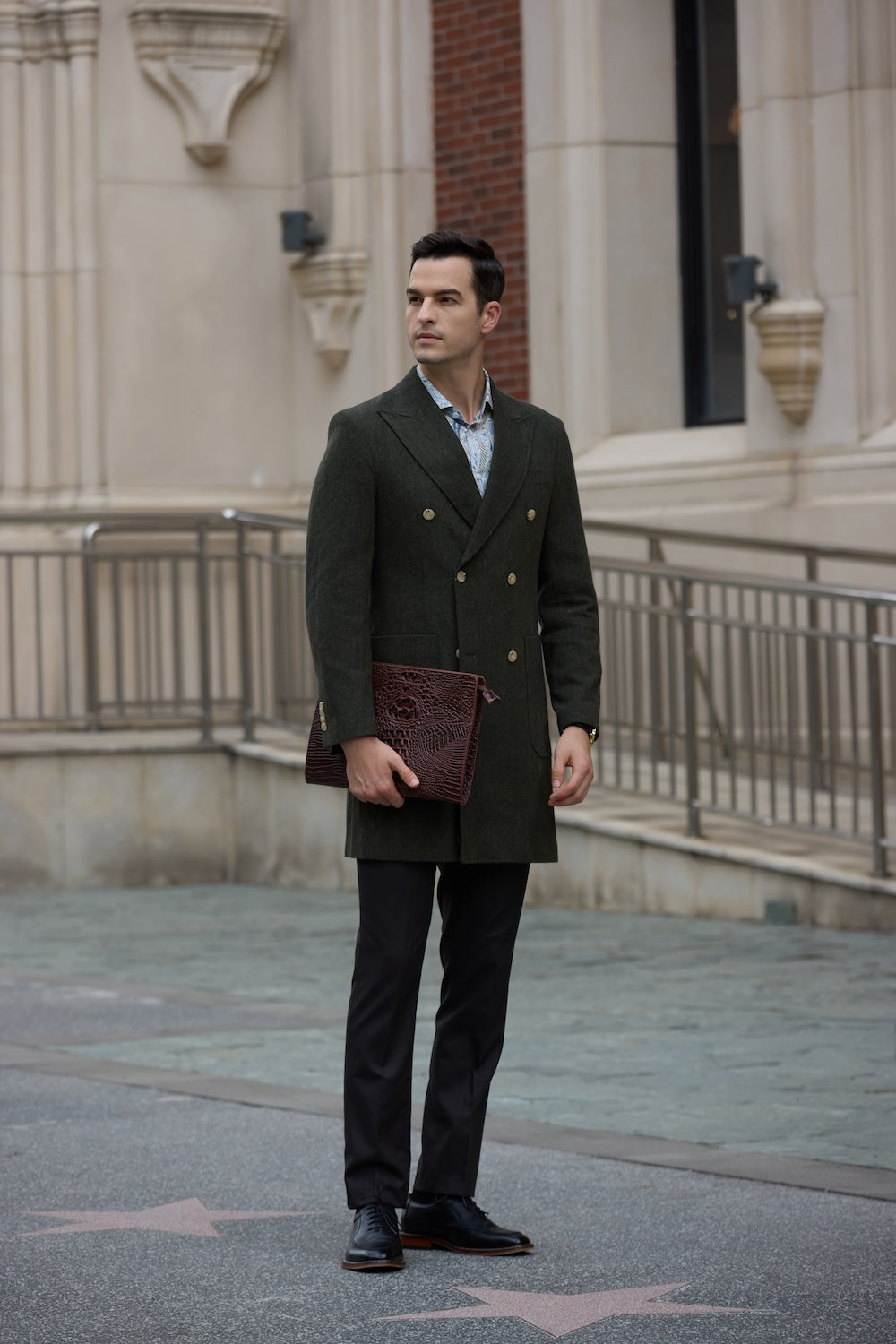Green dress overcoat styled with black pants and formal shoes in urban outdoor scene