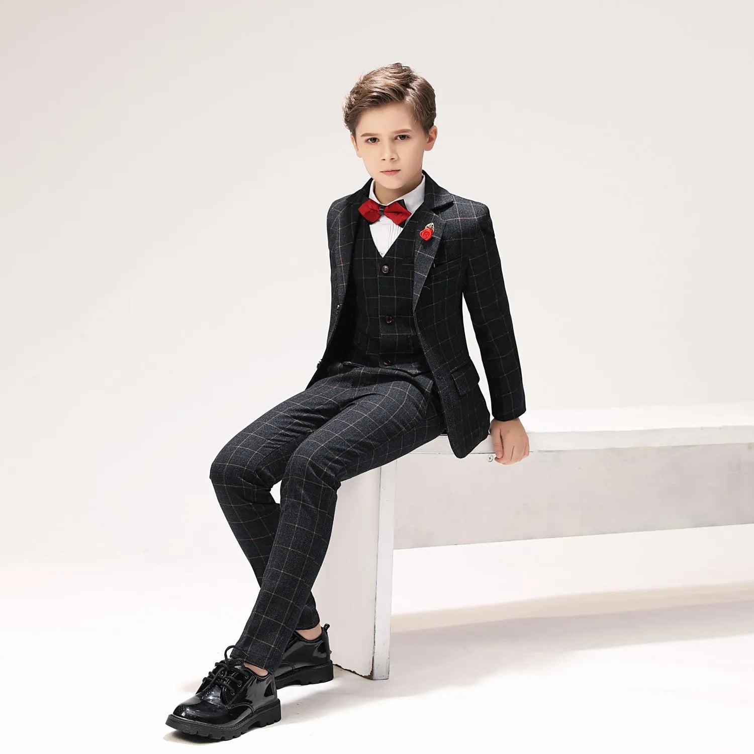Seated view of black plaid formal boys outfit with vest and jacket, perfect for photo shoot