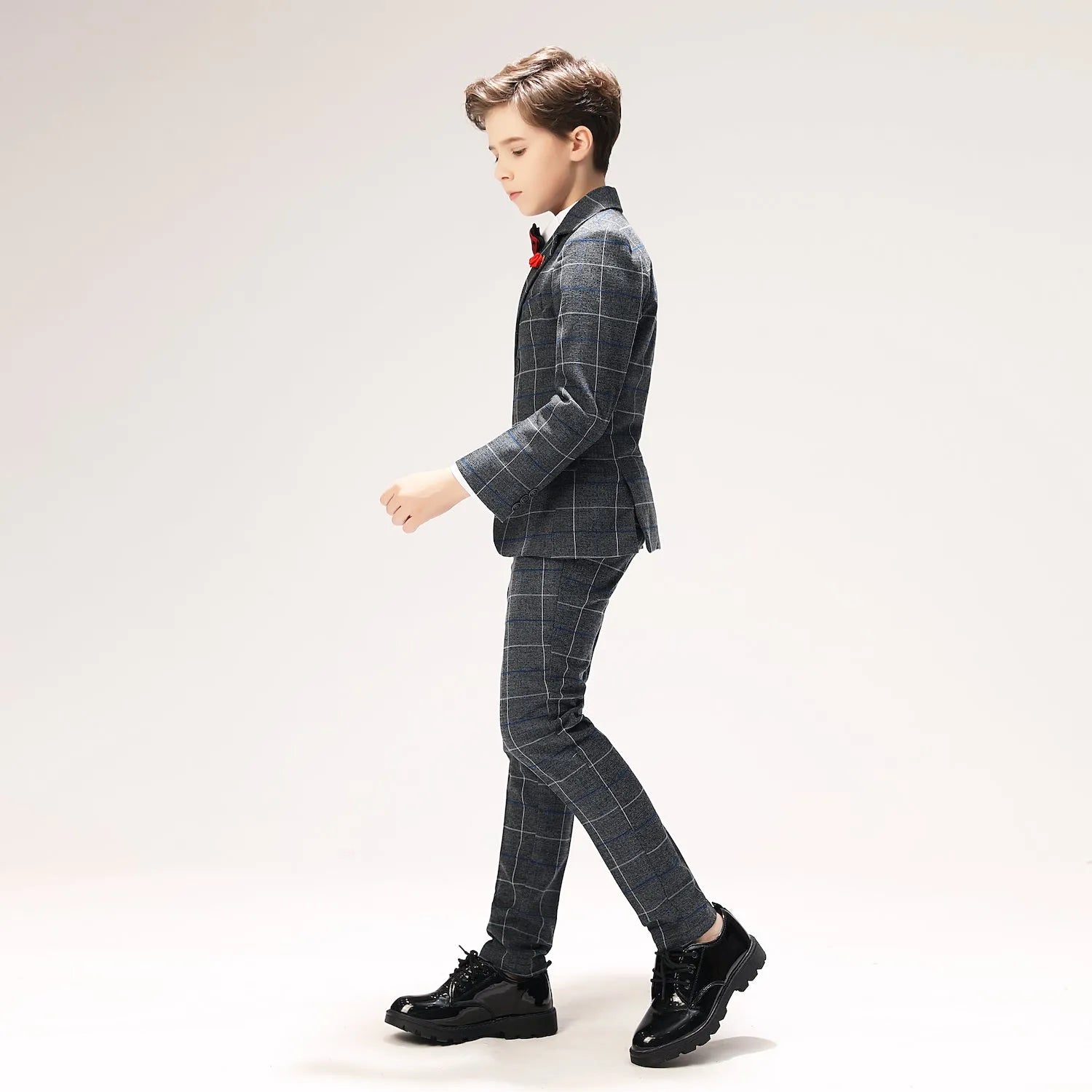 Walking pose in dark grey plaid 5-piece boys suit with classic polished shoes