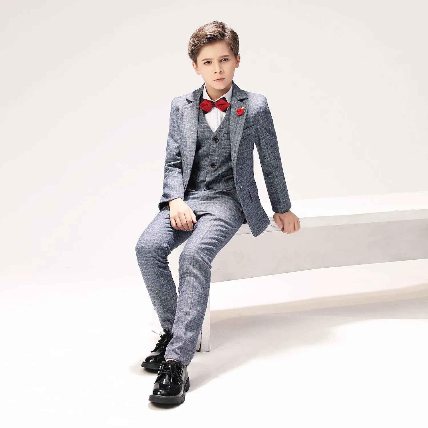 Seated pose showcasing full boys 5-piece plaid suit outfit for formal occasions or weddings