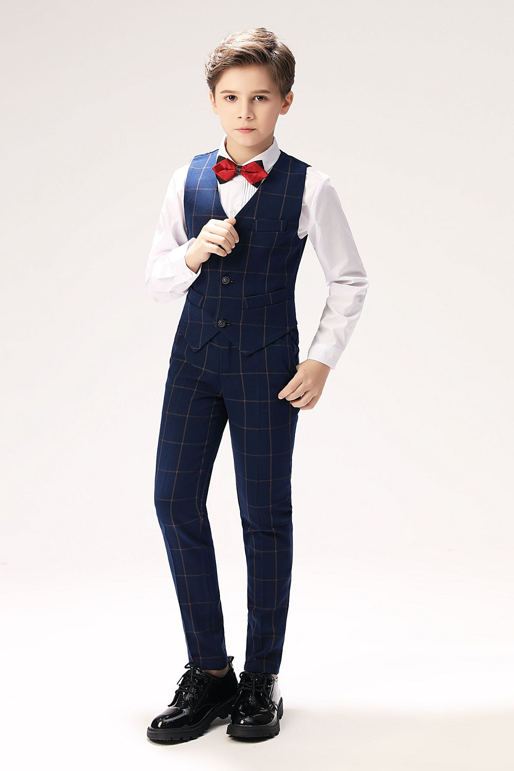 Full view of boy in navy plaid vest and pants with red bow tie, styled for special events