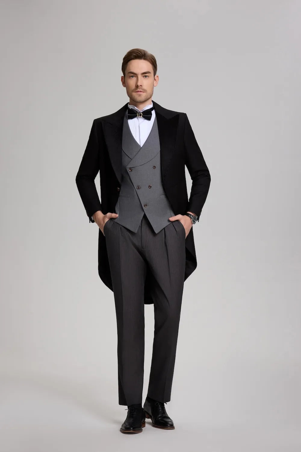 A man wearing a complete 3-piece evening suit, featuring a black peak lapel tailcoat and a grey double-breasted vest.