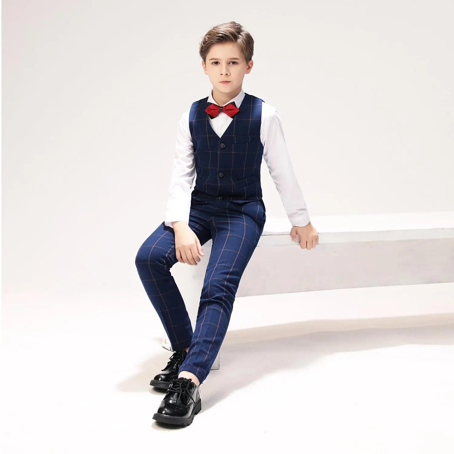 Boy seated in blue plaid formal suit with red bow tie for special occasions