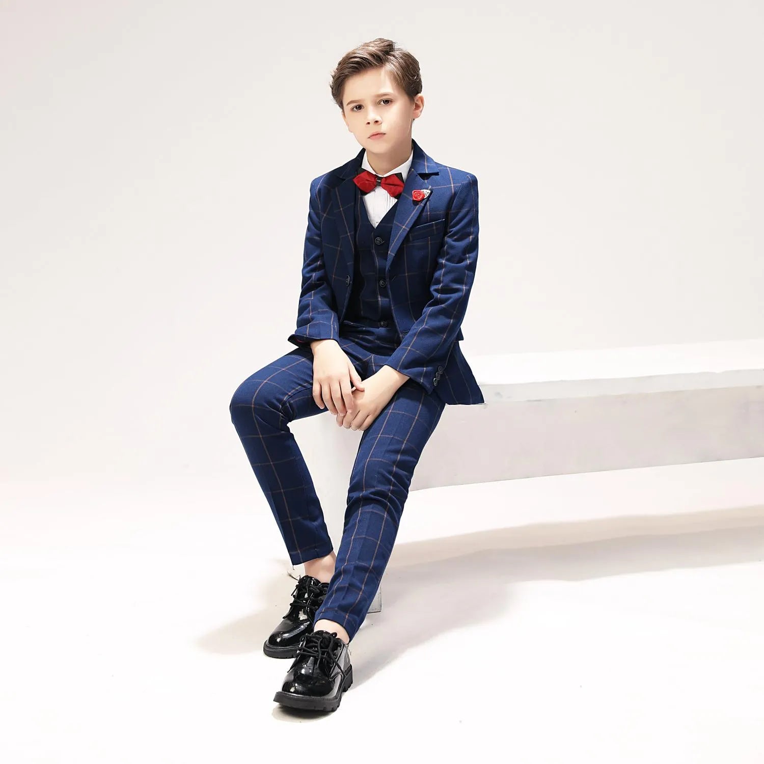 Three-piece boys plaid suit set styled with red accents and formal shoes