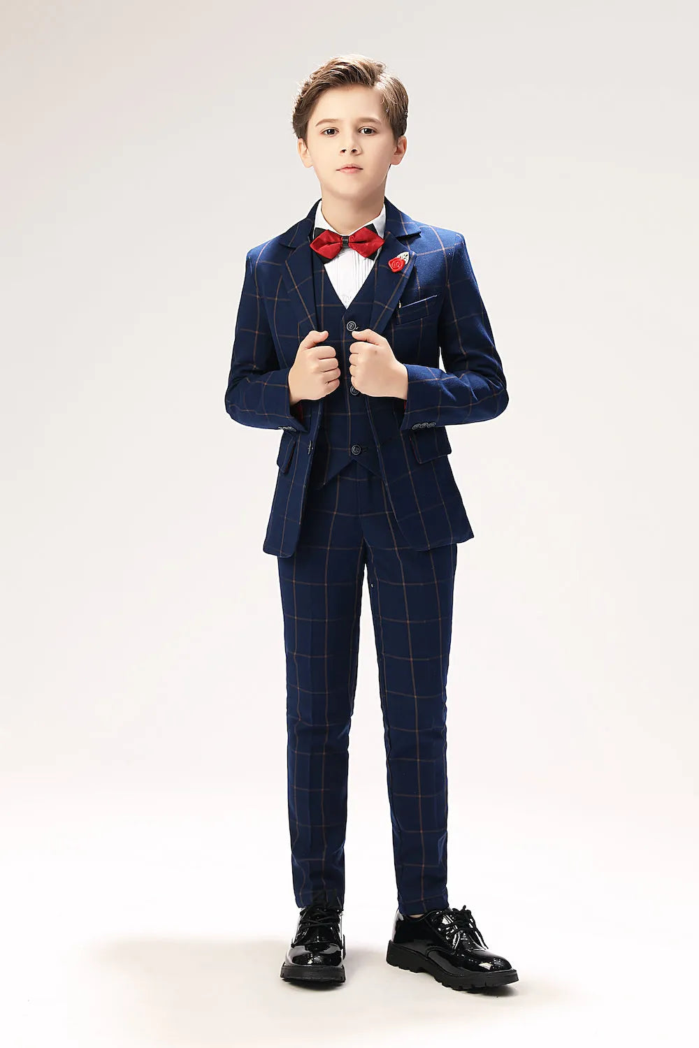 Boy wearing 5 piece blue plaid suit with red bow tie for formal events