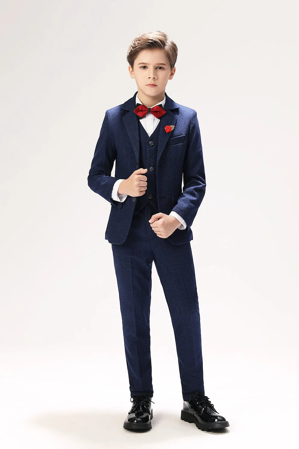 Boy in navy woolen 5-piece suit with red bow tie and lapel pin for formal prom or wedding look