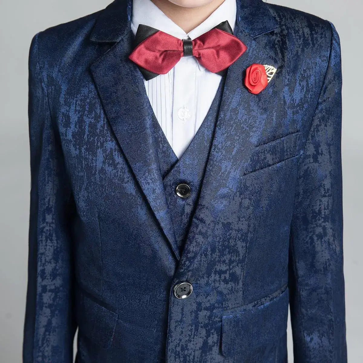 Close-up of boys' navy floral blazer with red bow tie and rose brooch, modern slim fit suit for formal occasions