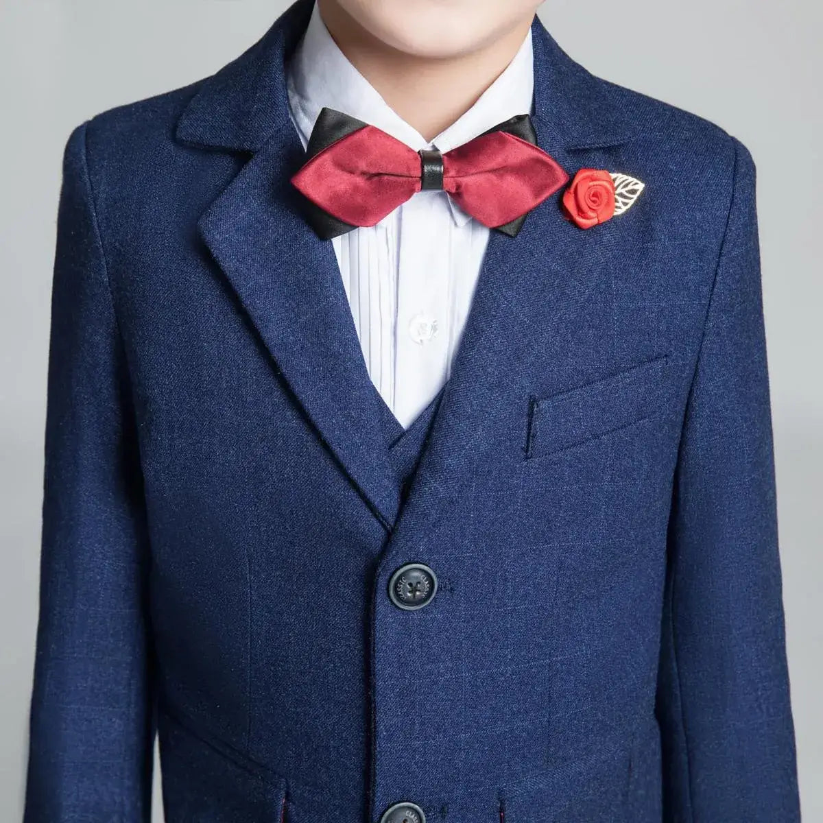 Close-up of red bow tie and rose pin on navy plaid boys blazer – stylish boys party outfit detail