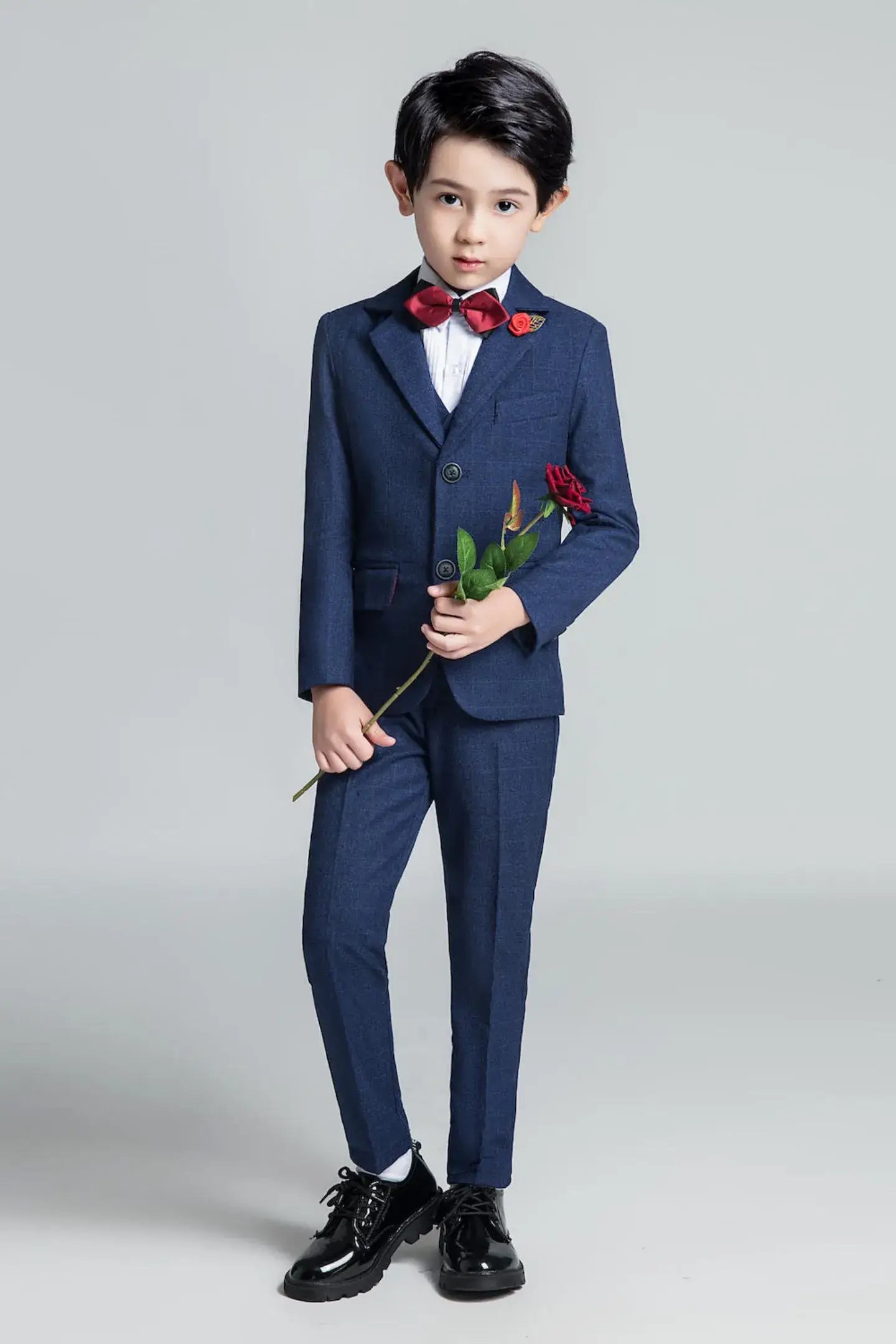Young boy in navy plaid 5-piece suit with red bow tie holding rose – holiday party outfit for boys