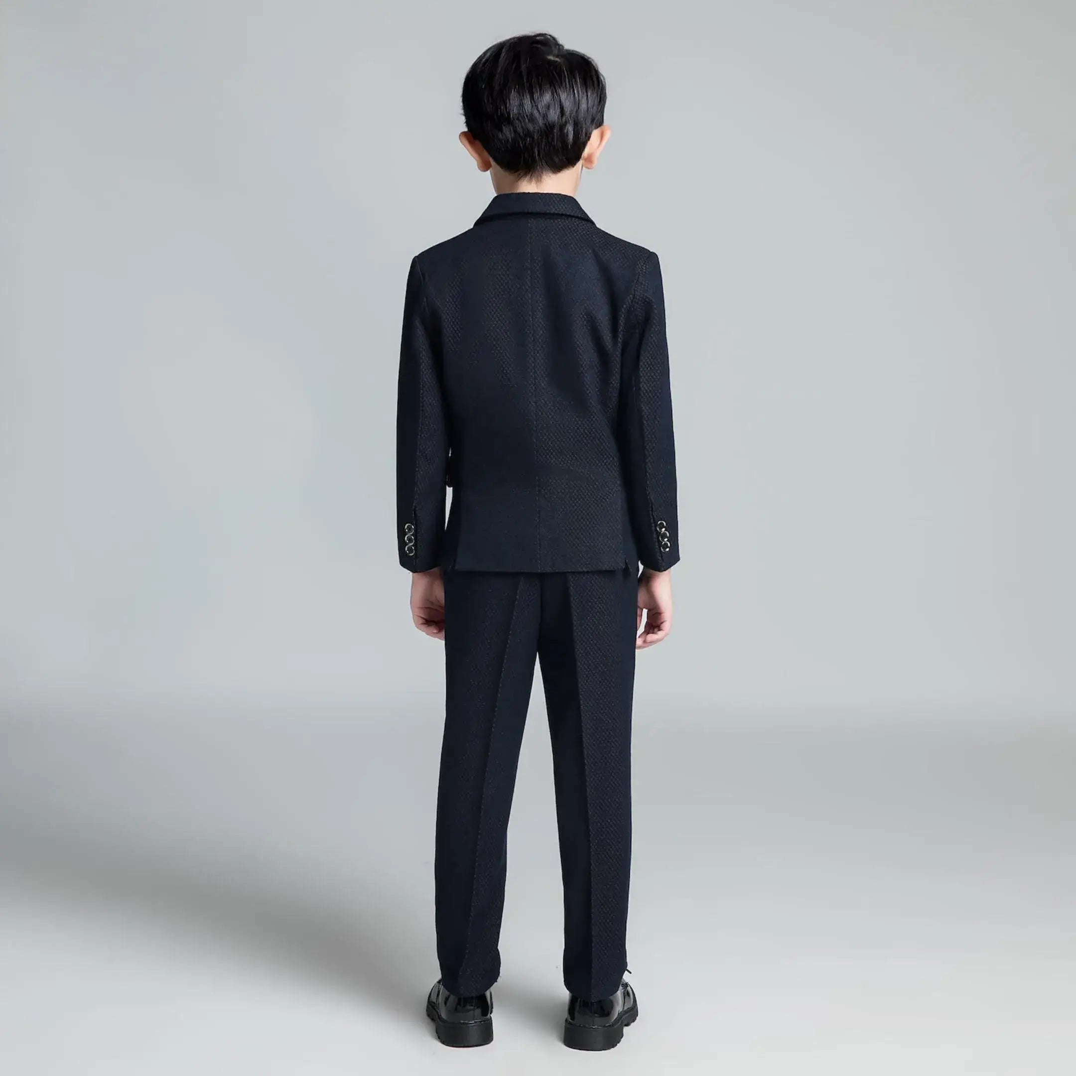 Back view of boys' slim fit formal suit with dark textured fabric and classic blazer cut for weddings and special events