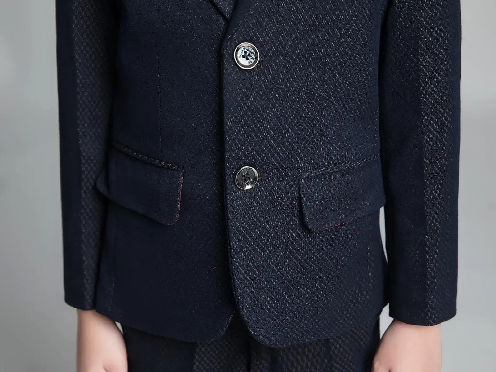 Close-up of boys' navy formal blazer with flap pockets, metallic buttons, and fine golden check pattern for elegant occasions