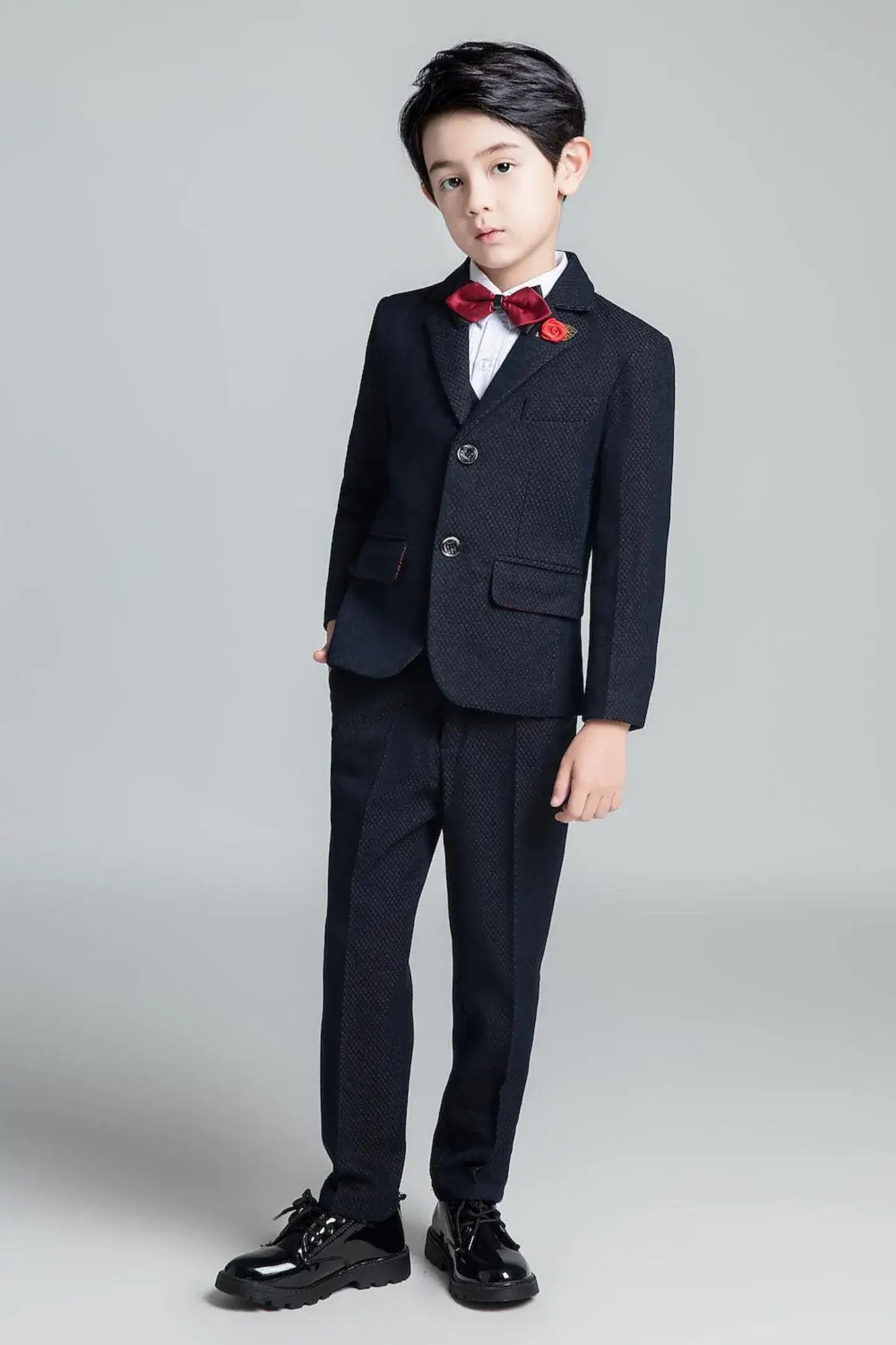 Dark navy boys' slim fit suit with subtle textured pattern and red bow tie, stylish formal wear for holiday events