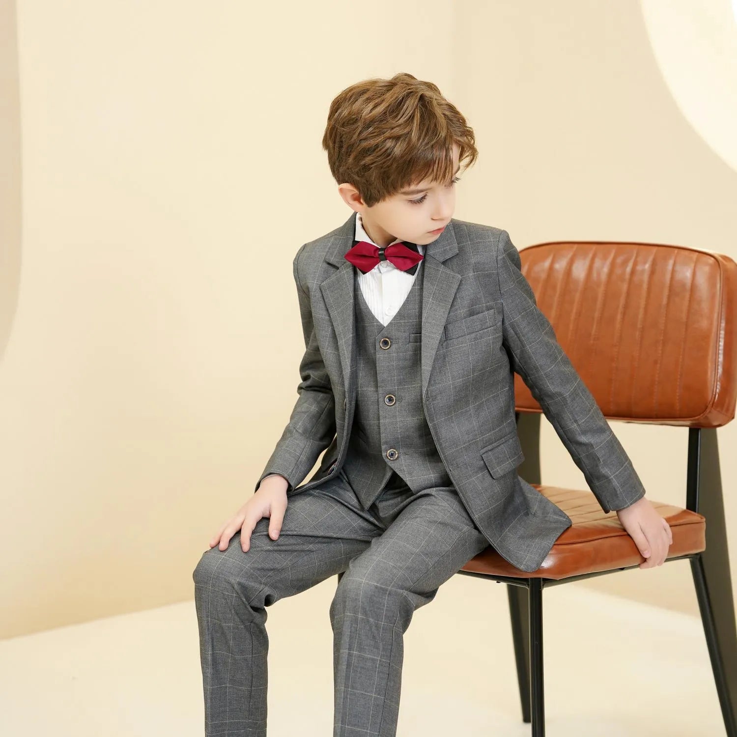 Grey plaid boys 5-piece suit: Seated pose with red bow tie & vest detail