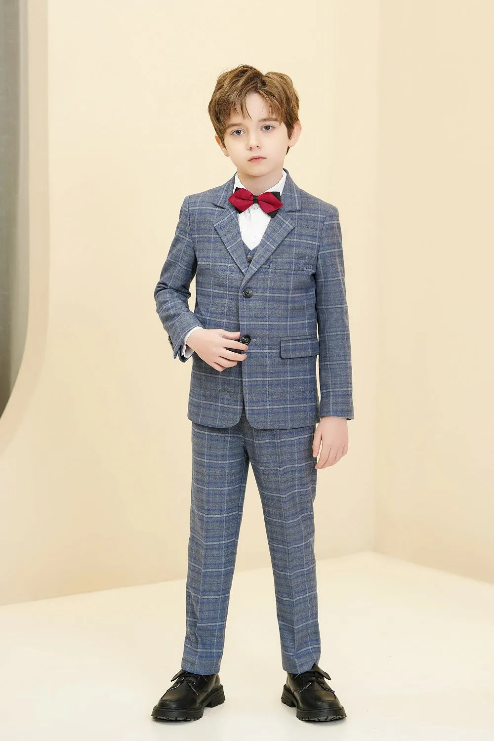 Boy in blue and white plaid 5 piece suit with red bow tie standing in formal pose.