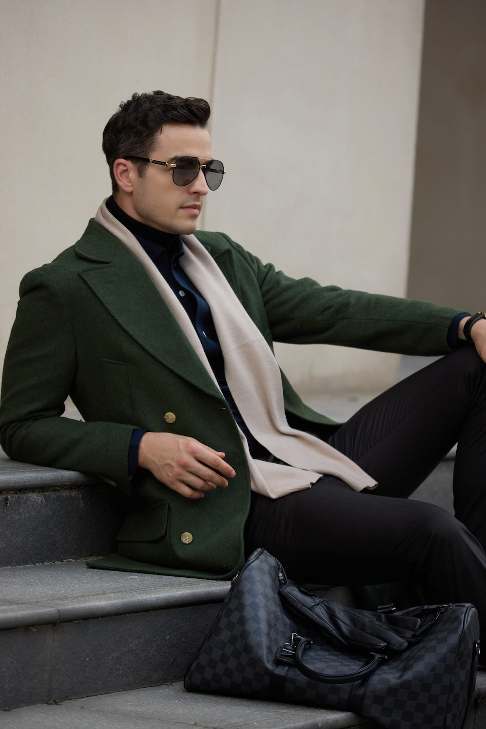 Man sitting in green overcoat with scarf and duffle bag – relaxed winter outfit