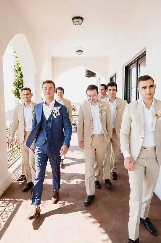 Groomsmen in beige linen 2 piece suits standing with groom in blue three piece suit at summer wedding