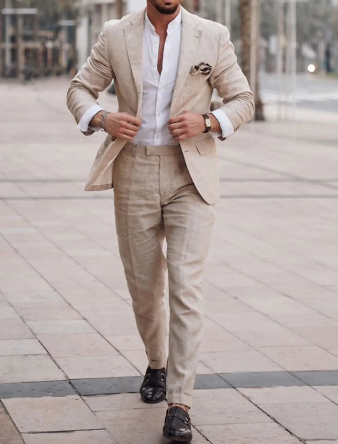 Full-body view of man wearing beige linen wedding suit walking on tiled street