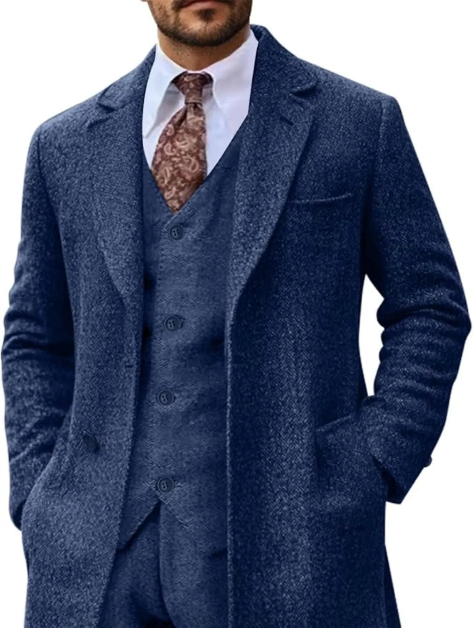 model wearing navy herringbone 3 piece suit with long tweed blazer, white shirt and patterned tie, hands in pockets for a formal look.