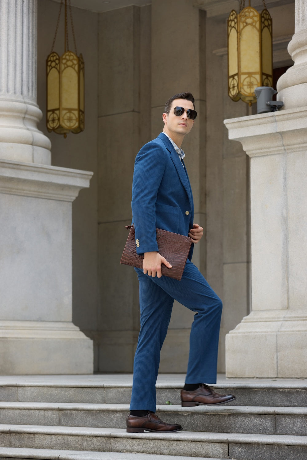 Royal blue corduroy suit in motion – man walking upstairs with brown clutch and polished shoes