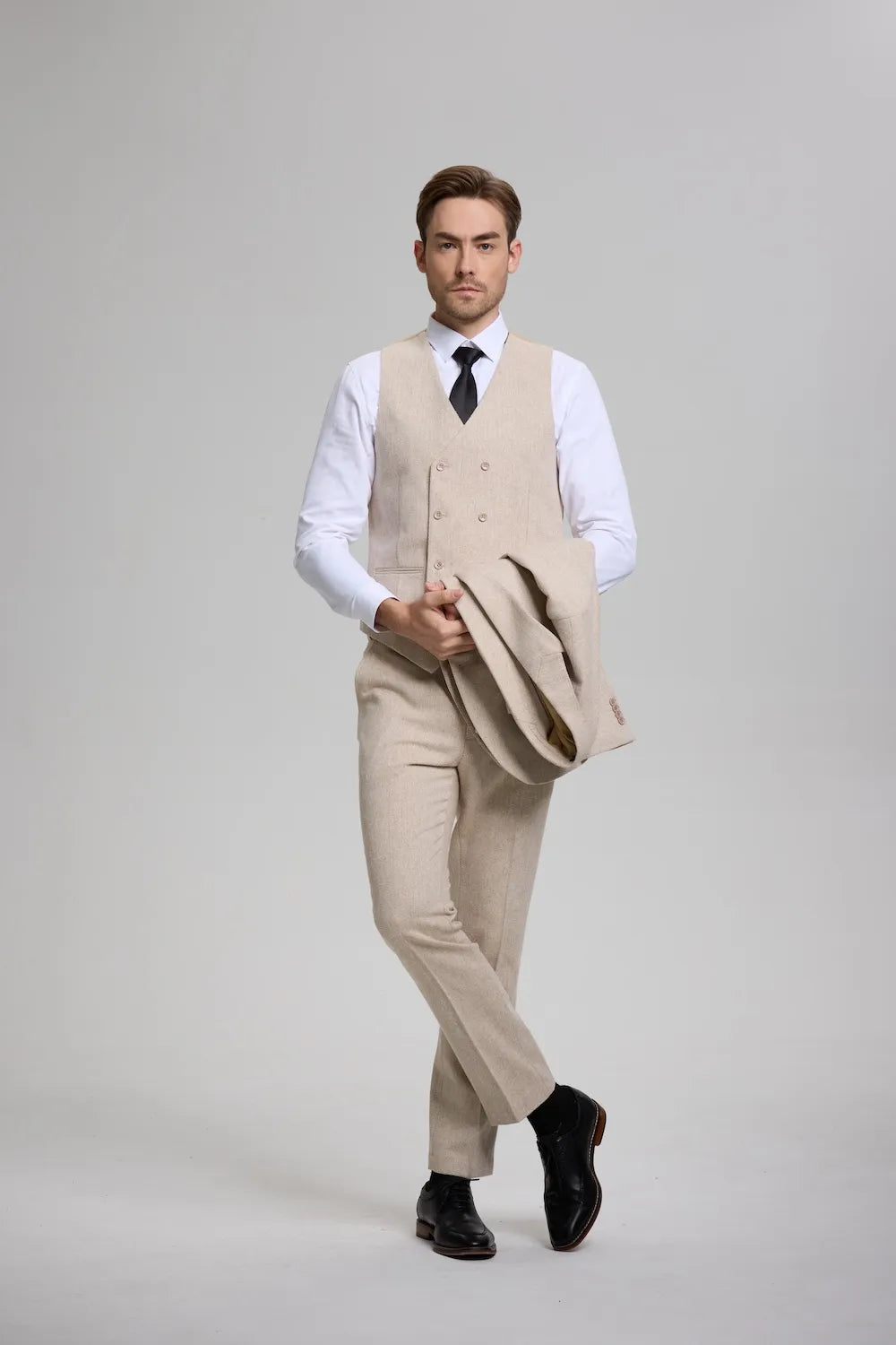 Man in a champagne herringbone 3-piece suit waistcoat, paired with tailored trousers and formal accessories.