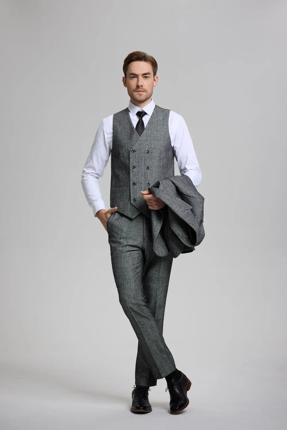 Man in a dark gray herringbone 3-piece suit waistcoat, paired with tailored trousers and formal accessories.