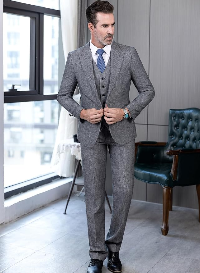Modern groom style in grey tweed herringbone 3 piece suit for men, worn with blue tie and white shirt indoors