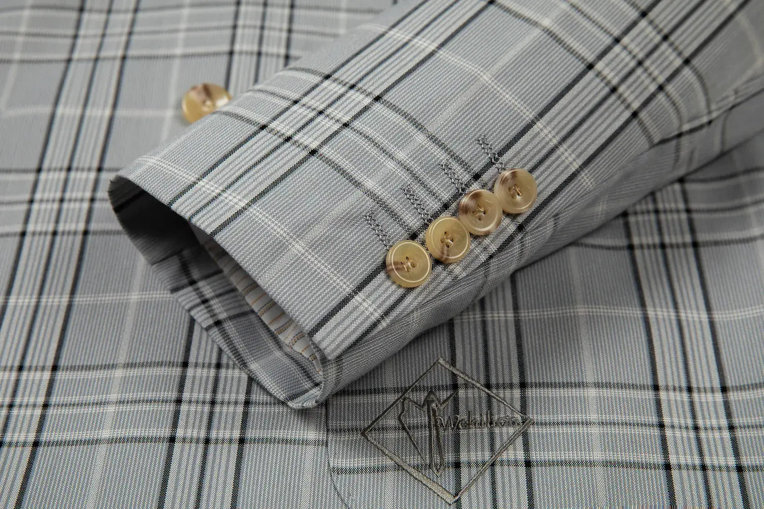 Close-up of blazer cuff with four beige buttons on grey plaid fabric.