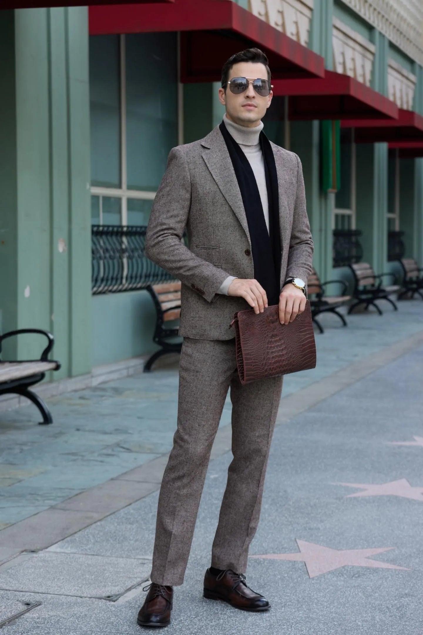 front view of men's brown tweed herringbone 2-piece suit with black scarf, featuring a slim fit business style, paired with dress shoes and a leather clutch.