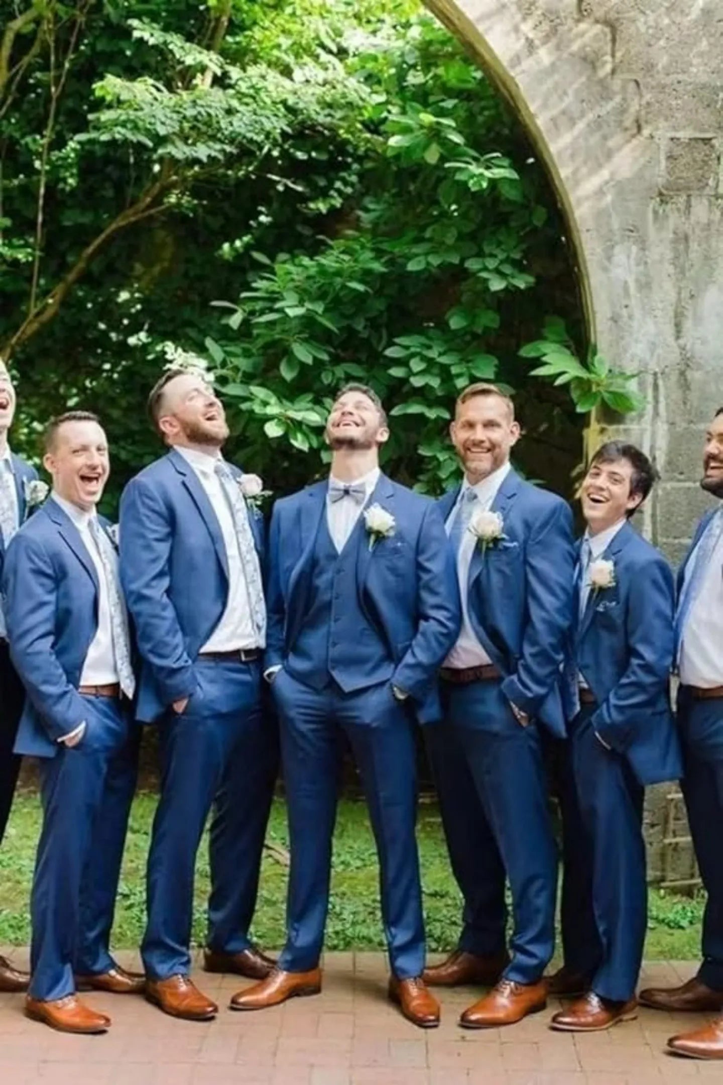 group of groomsmen in wine red suits laughing casually outdoors during wedding photoshoot